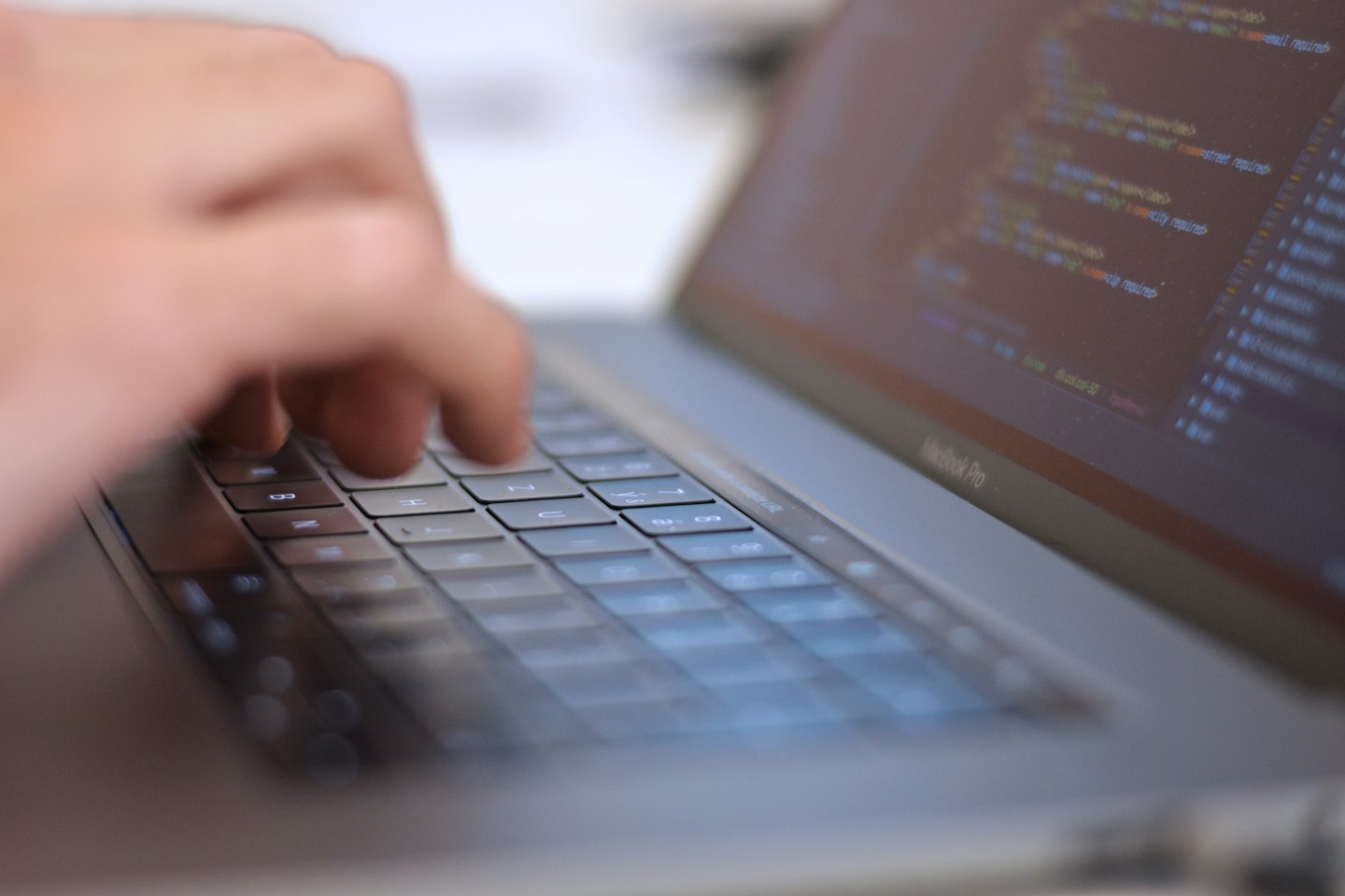 Hands typing lines of programming code on a laptop keyboard.