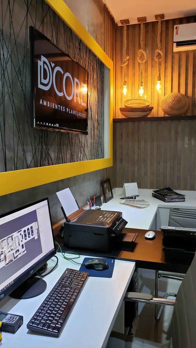 Modern office with desks, computers displaying floor plans and D'CORE logo.