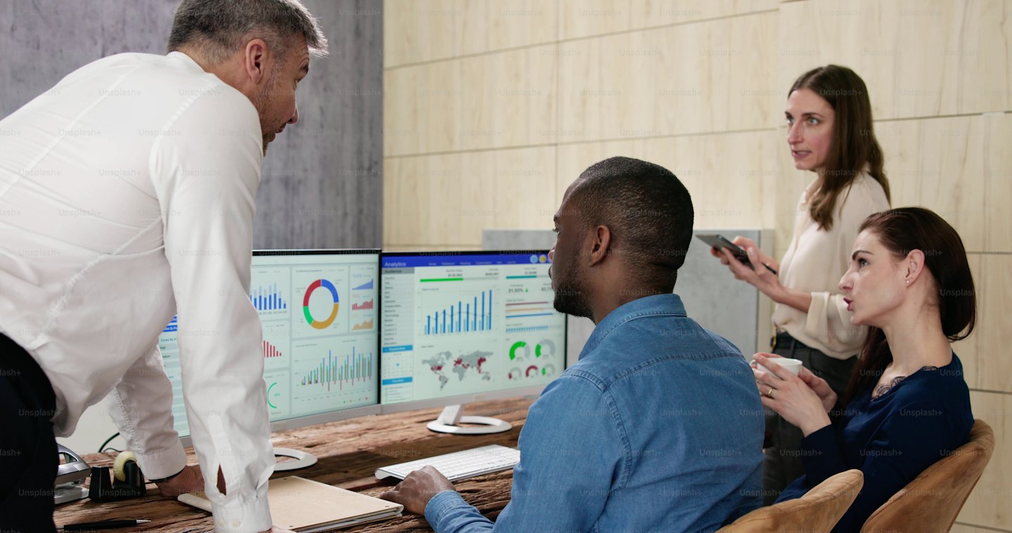 Business professionals collaborate while analyzing data on computer monitors.